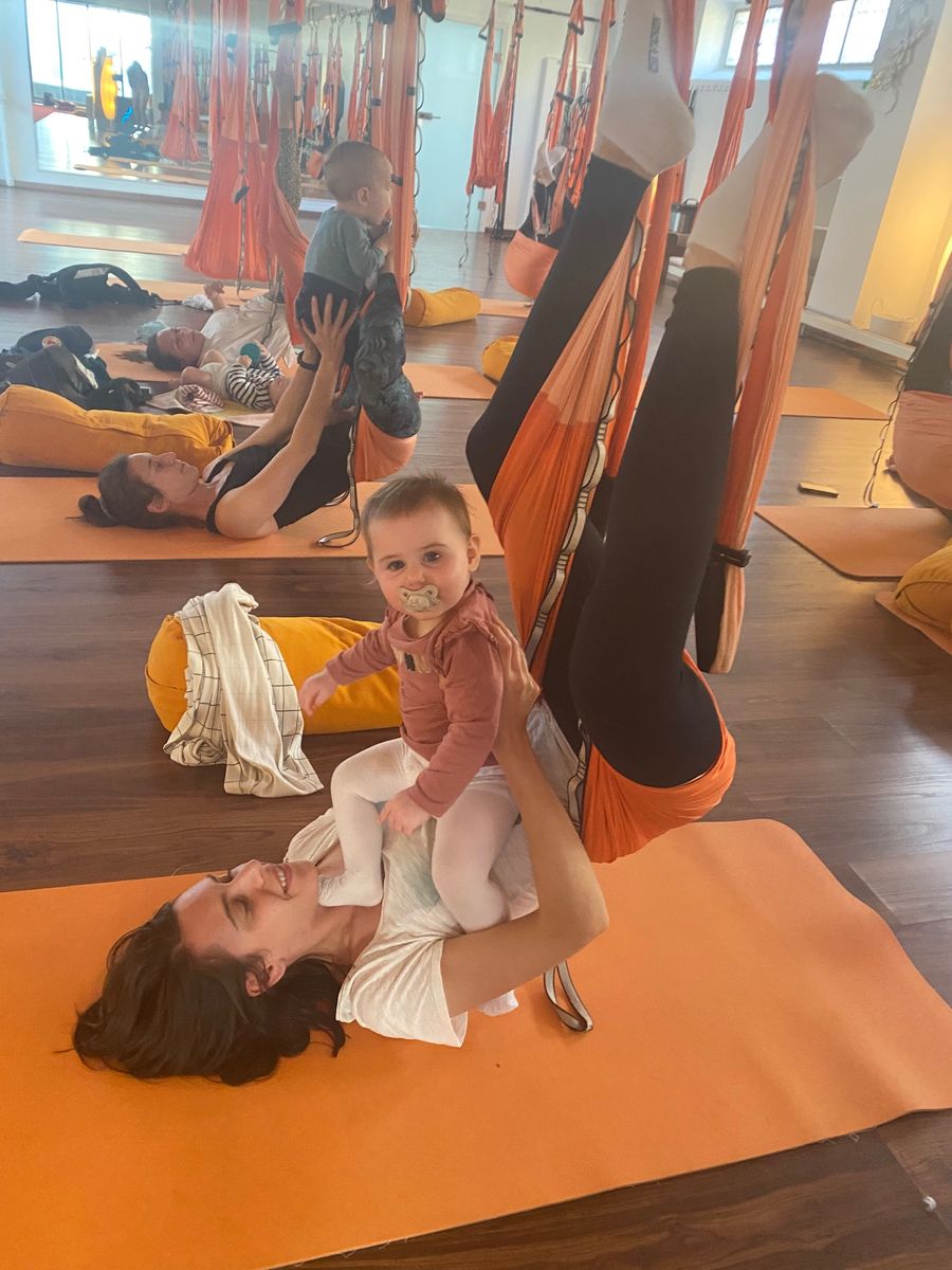 Aula com bebés: mães deitadas no tapete, pernas no tecido, bebés ao colo